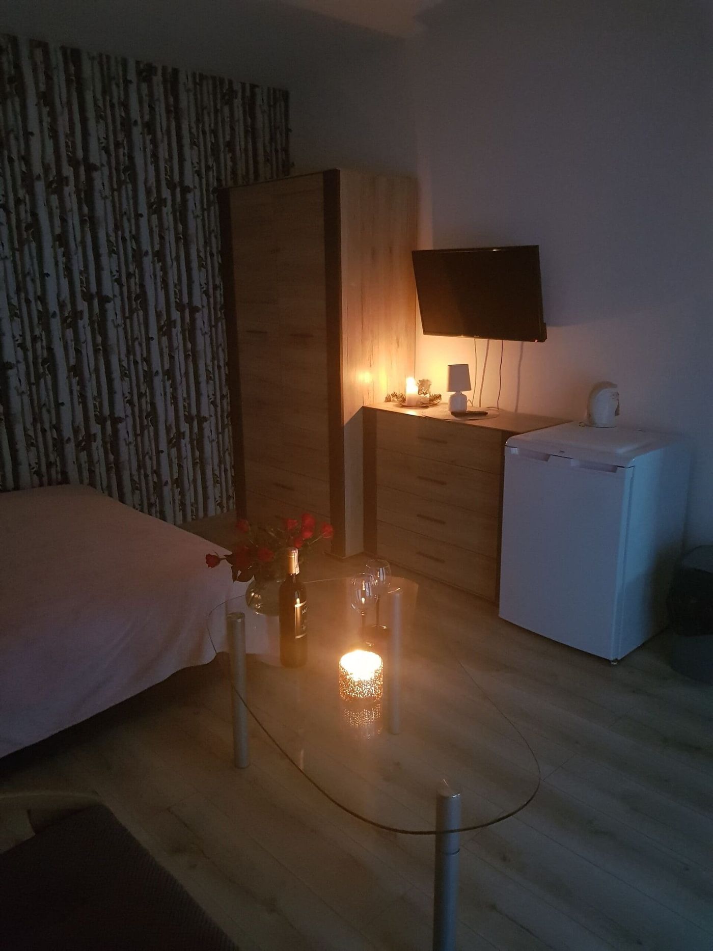 Pokój z telewizorem, komodą i lodówką, wieczorem przy świecach